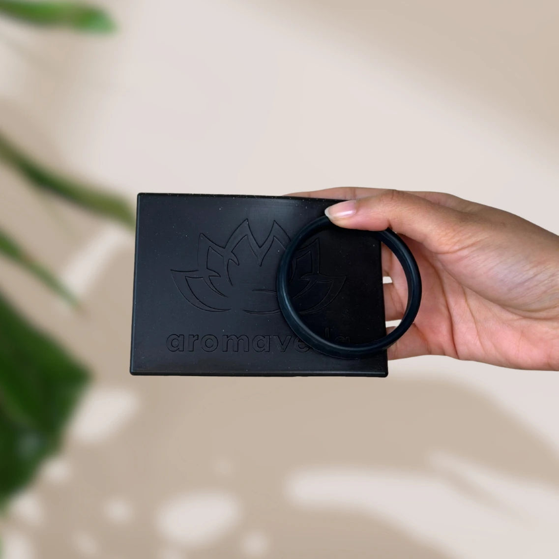 Schwarze Aromaveda Platte mit Lotus-Blumen und aromaveda Gravur und schwarzes Armband gehalten von einer Hand