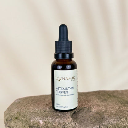 Braune Tropfenflasche mit DYNAMIKPLUS "Astaxanthin Tropfen" Etikett auf Stein