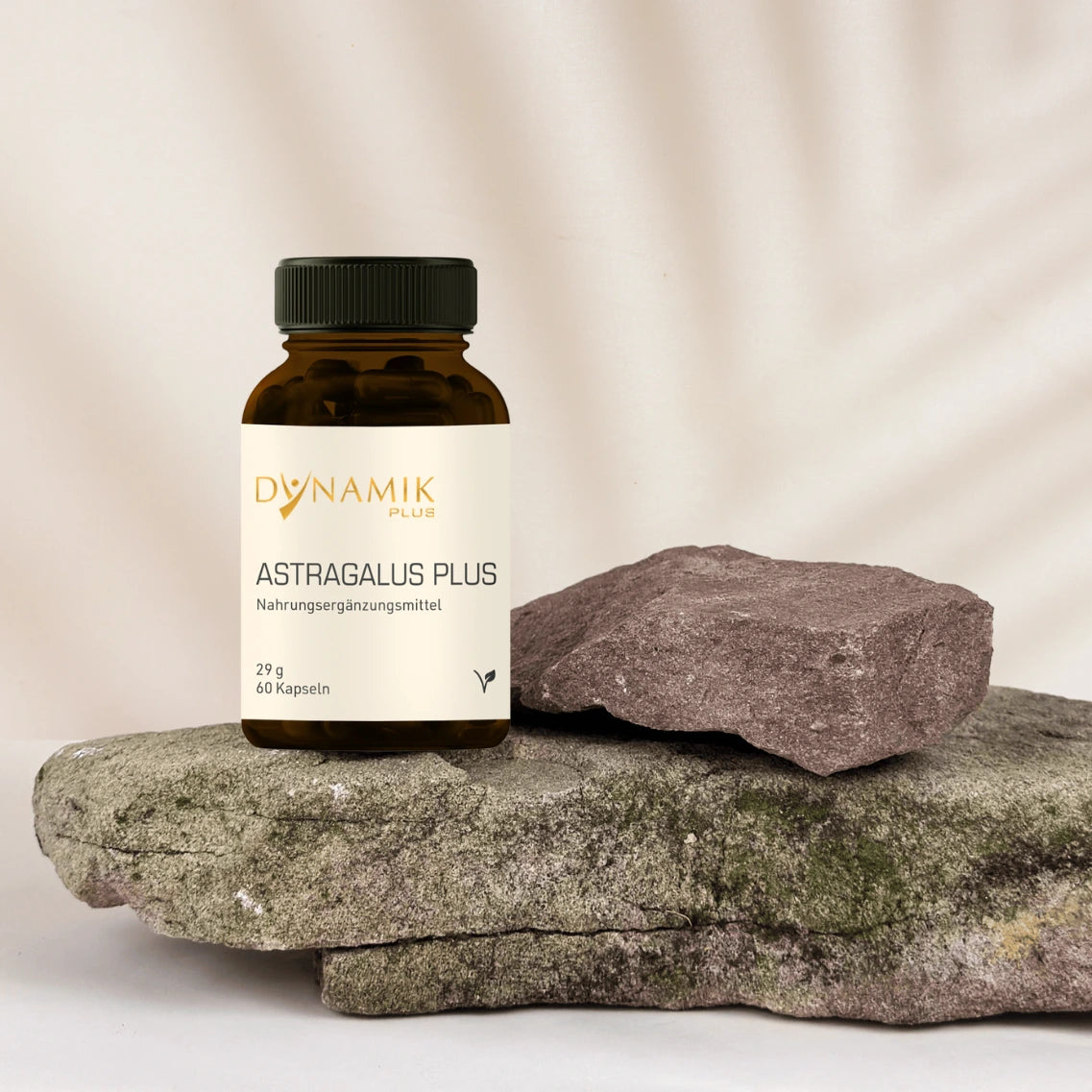 Brauner Glasbehälter mit DYNAMIKPLUS "Astragalus Plus" Etikett und schwarzen Drehverschluss auf Stein