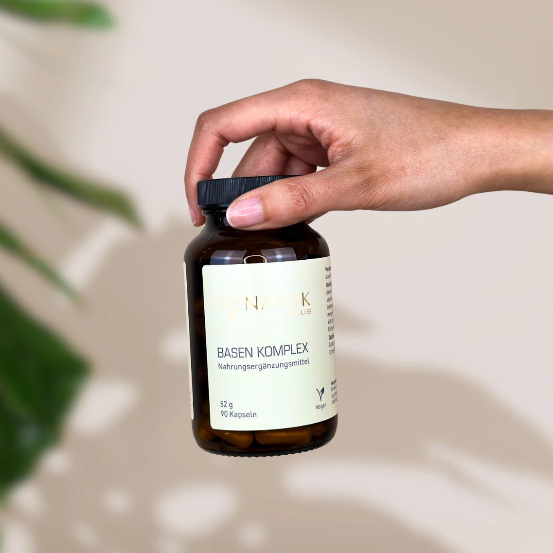 Brauner Glasbehälter mit DynamikPlus "Basen Komplex" Etikett und schwarzem Drehverschluss gehalten in einer Hand