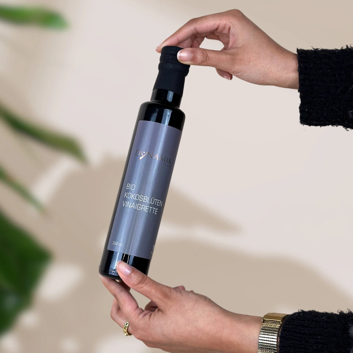 Braune kleine Ölflasche mit DynamikPlus "Bio Kokosblüten Vinaigrette" Etikett gehalten