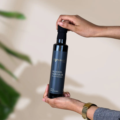 Braune kleine Ölflasche mit DynamikPlus "Bio Kokoswürzsauce" Etikett gehalten