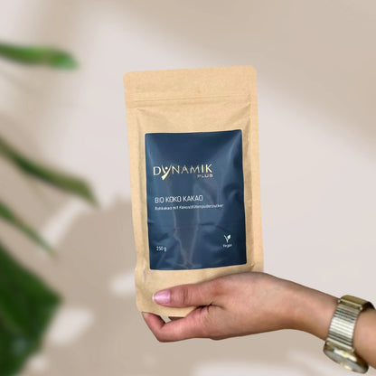 Beiger Kartonbeutel mit DynamikPlus "Bio Koko Kakao" Etikett gehalten in Hand