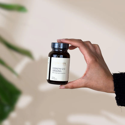 Brauner Glasbehälter mit DynamikPlus "Coenzym Q10 Ubiquinol" Etikett und schwarzem Drehverschluss gehalten von einer Hand