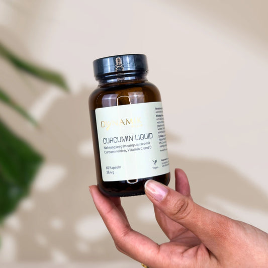 Brauner Glasbehälter mit DynamikPlus "Curcumin Liquid" Etikett und schwarzem Drehverschluss gehalten von einer Hand