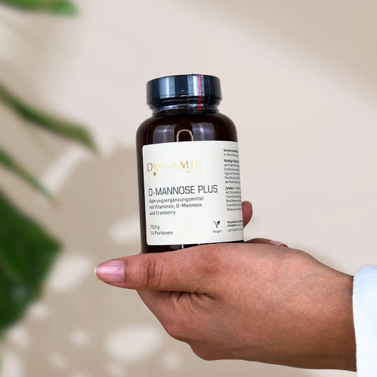 Brauner Glasbehälter mit DynamikPlus "D-Mannose Plus" Etikett und schwarzem Drehverschluss gehalten in Hand