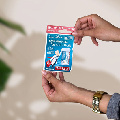 Blaue Verpackung mit "Dr. Skin Hautpuder" Druck und Arztabbildung, gehalten von zwei Händen