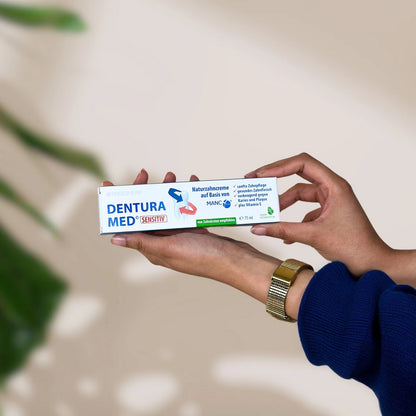 Rechteckige weiß-blaue Verpackung mit "Froximun DENTURA MED Zeolith" Print und Zahn auf Verpackung, gehalten 