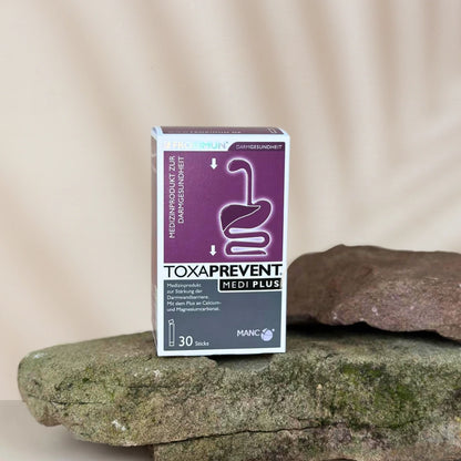 Rechteckige violet-weiße Verpackung mit "TOXAPREVENT Medi Plus mit Zeolith" Print und Verdauungstraktabbildung auf Stein
