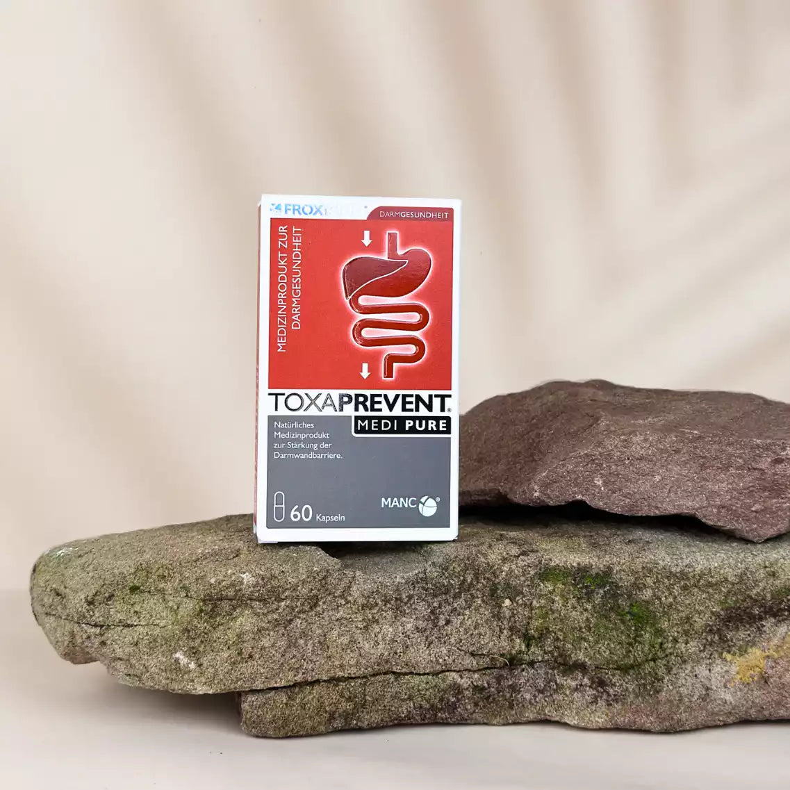 Rechteckige rot-weiße Verpackung mit "TOXAPREVENT Medi Pure 60 Kapseln" Print auf Stein