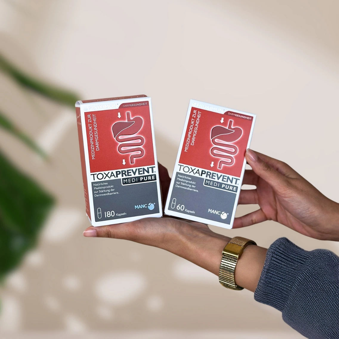 Rechteckige rot-weiße Verpackung mit "TOXAPREVENT Medi Pure" Print und Verdauungstraktabbildung große und kleine Packung in Hand gehalten
